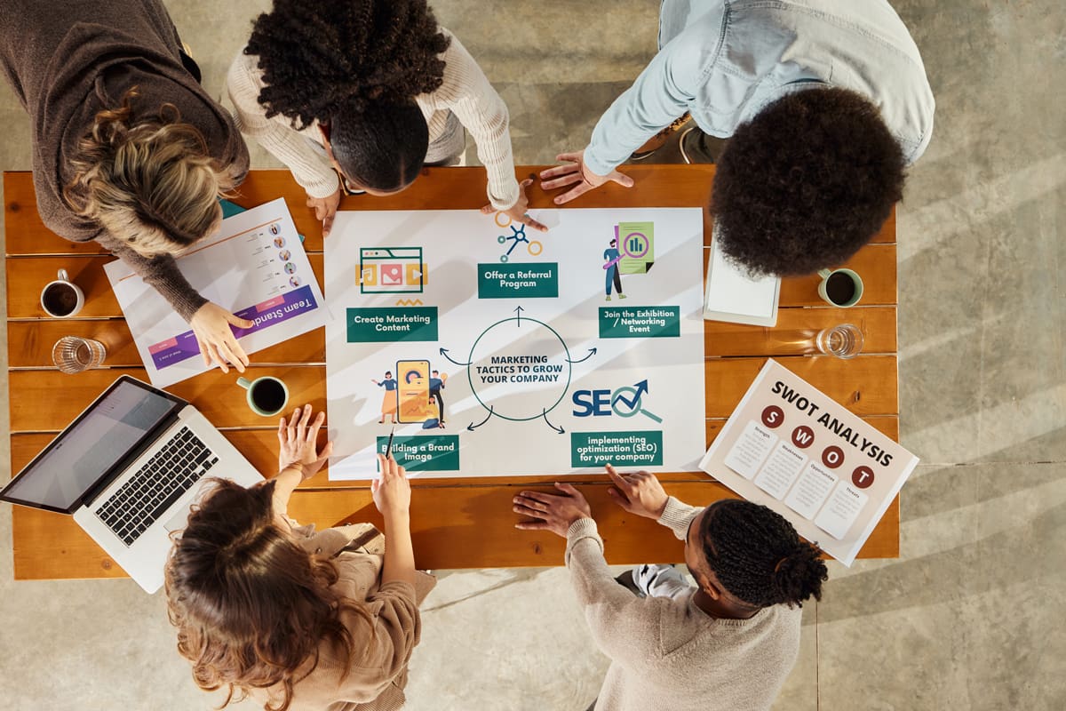 Digital-Marketing-Team High angle view of team of creative people cooperating while analyzing marketing tactics for expanding a company in the office.
